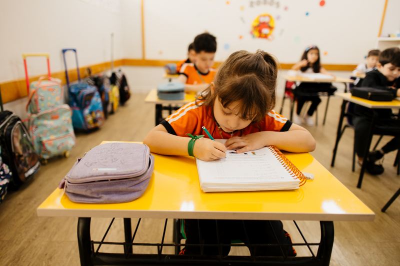 Menina escrevendo no caderno em sala de aula