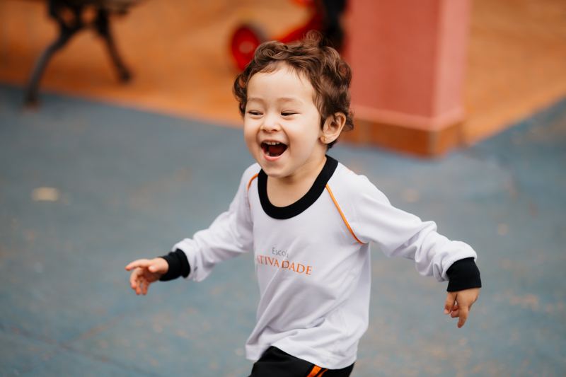 Menino correndo e rindo no pátio da Educação Infantil