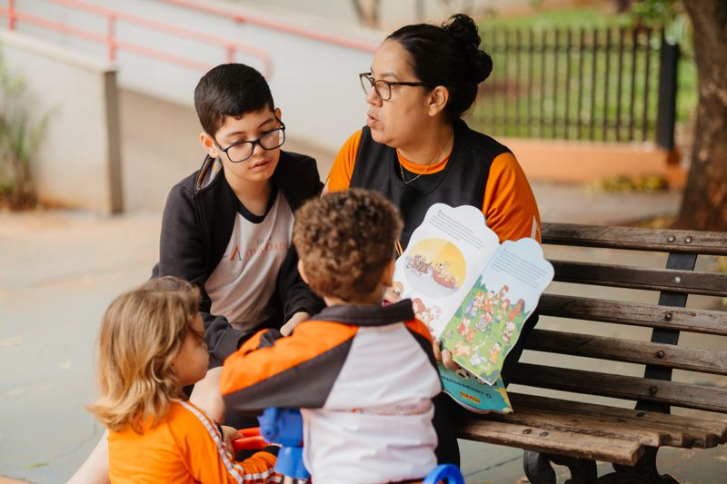 Educadora lendo um livro com os alunos no pátio